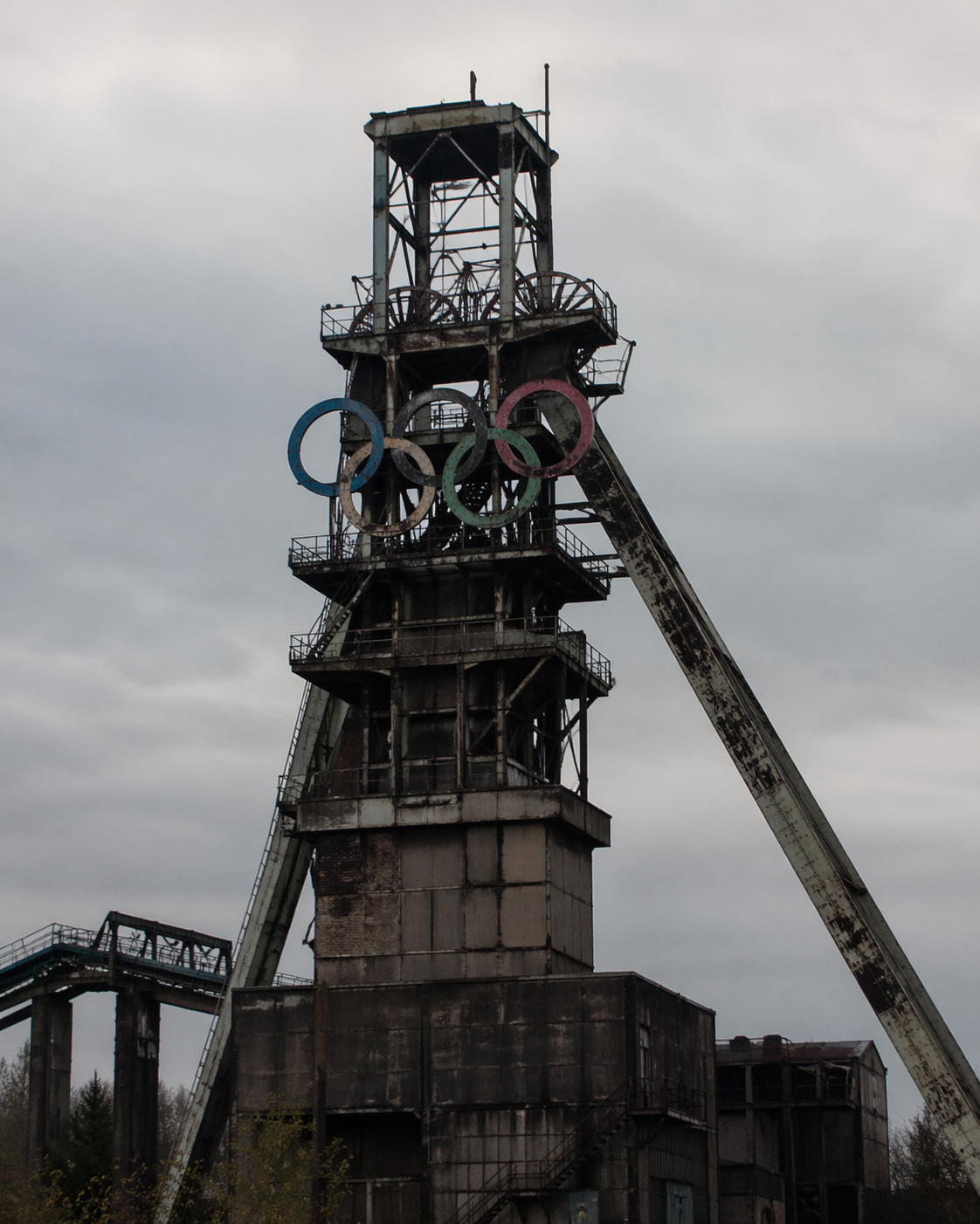 Ein verfallener Förderturm mit den Olympischen Ringen vor einem grauen Himmel