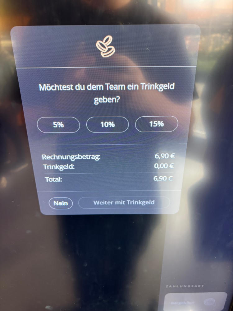 Zahlungsdisplay mit Trinkgeldabfrage auf Deutsch. Rechnung: 6,90 €. Auswahl: 5 %, 10 % oder 15 % Trinkgeld. Aktuell: 0,00 € Trinkgeld, Gesamtbetrag 6,90 €. Unten die Optionen „Nein“ und „Weiter mit Trinkgeld“.